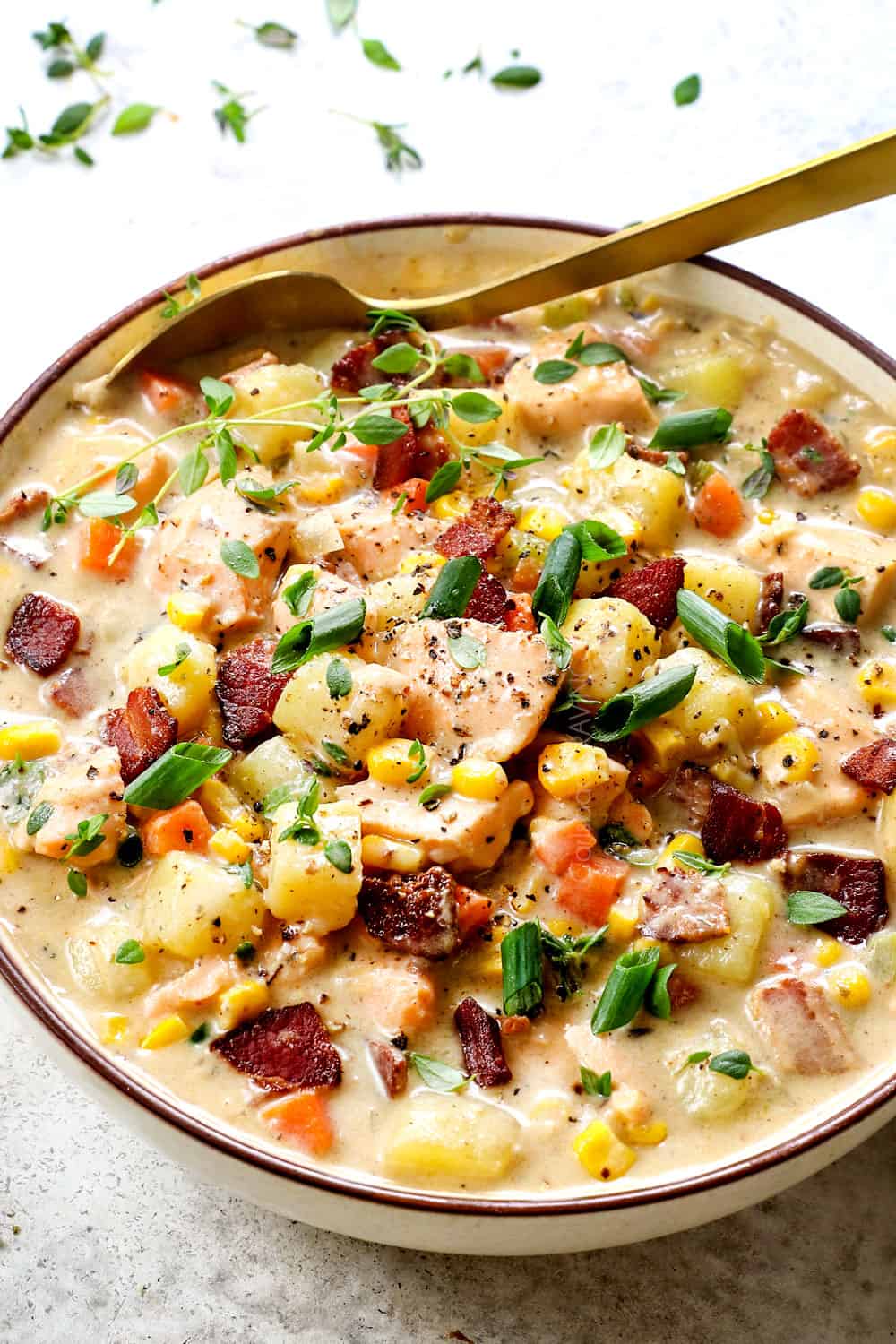 a bowl of salmon chowder recipe (fish chowder) showing how to serve it by garnishing with green onions, crispy bacon and fresh thyme