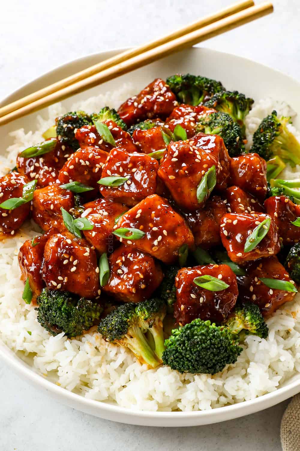 showing how to serve honey sesame chicken recipe by adding to a bowl with rice 
