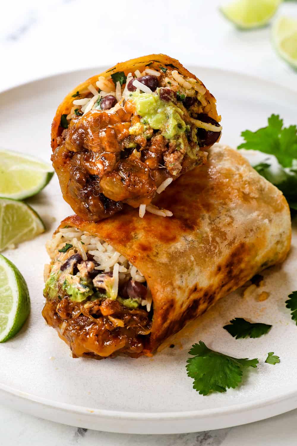 beef burrito recipe cut in half showing the filling with ground beef, rice, beans, sour cream and guacamole