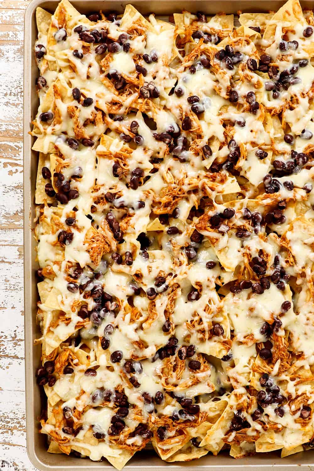 showing how to make shredded chicken nachos recipe by melting cheese over nachos in the oven