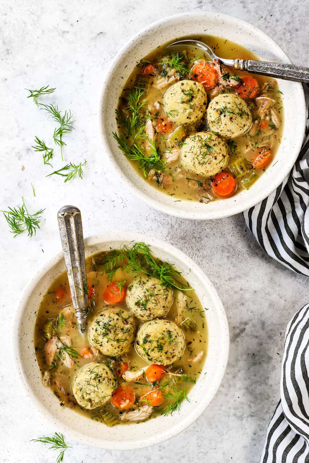 top view of matzo ball soup in two bowls garnished with dill