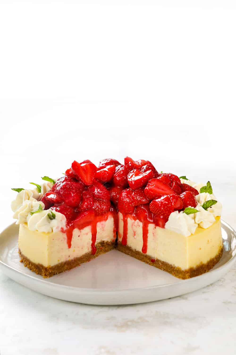 front view of strawberry cheesecake with slices missing showing the strawberry topping and rich cheesecake
