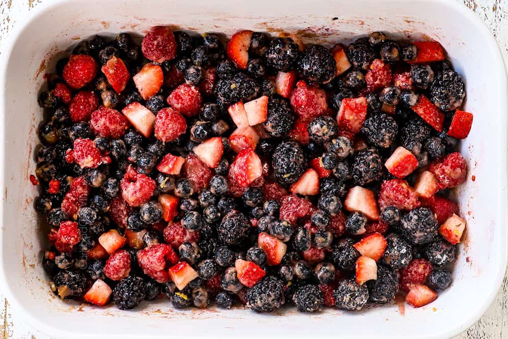 showing how to make berry cobbler recipe by spreading mixed berries into a baking dish