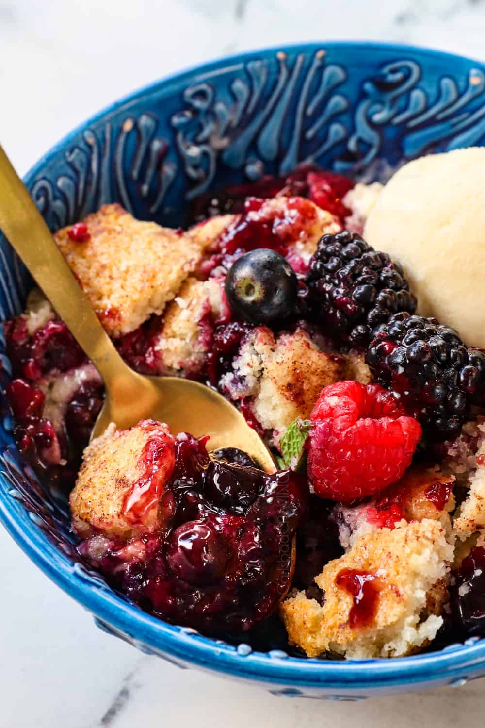 up close of a spoonful of with blackberries, blueberries, raspberries and strawberries mixed berry cobbler