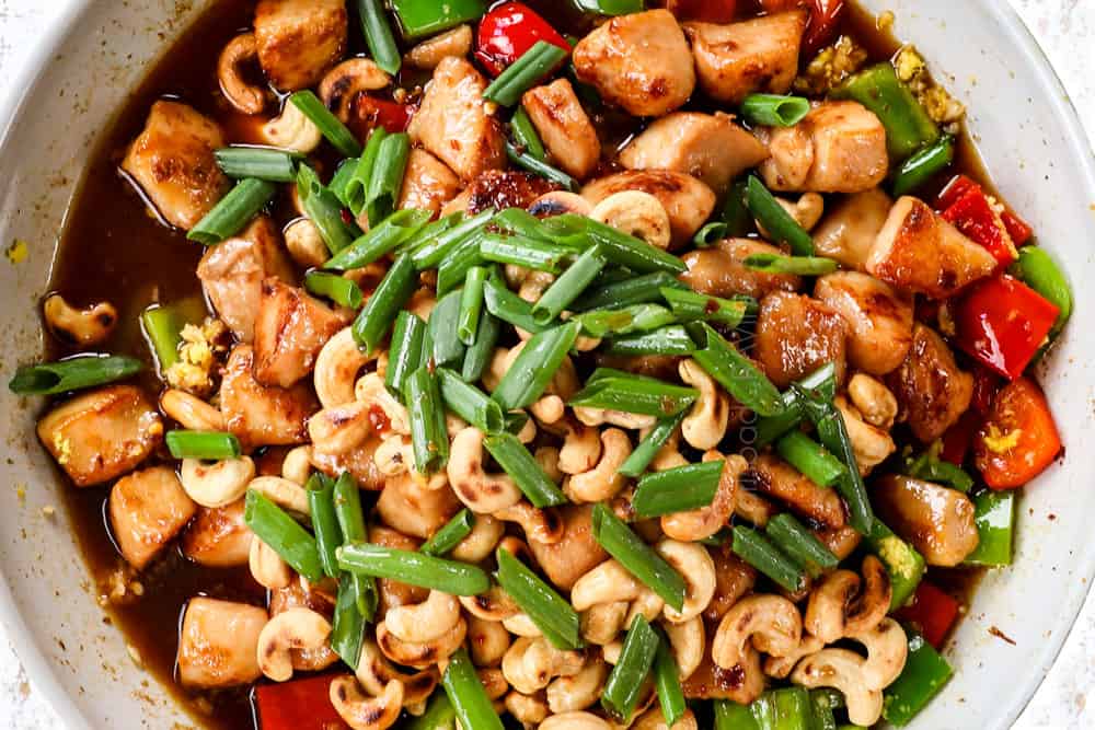 showing how to make cashew chicken recipe by adding stir fry sauce, cooked chicken, cashews and green onions to the bell peppers in the skillet to simmer