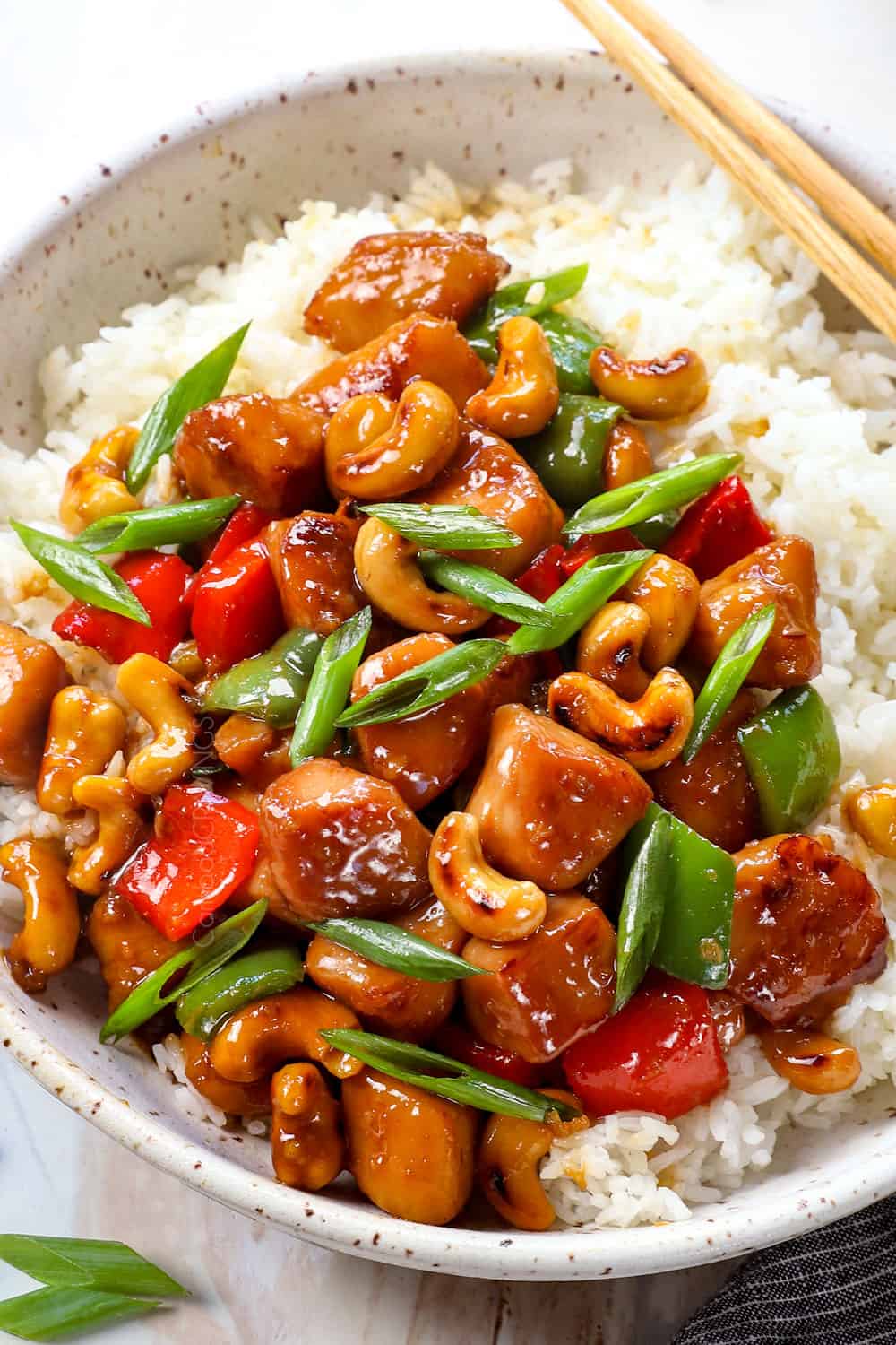 showing how to serve cashew chicken by serving on a bowl of rice with chopsticks