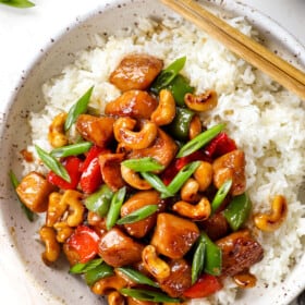 showing how to serve cashew chicken recipe on a white rice garnished with green onions
