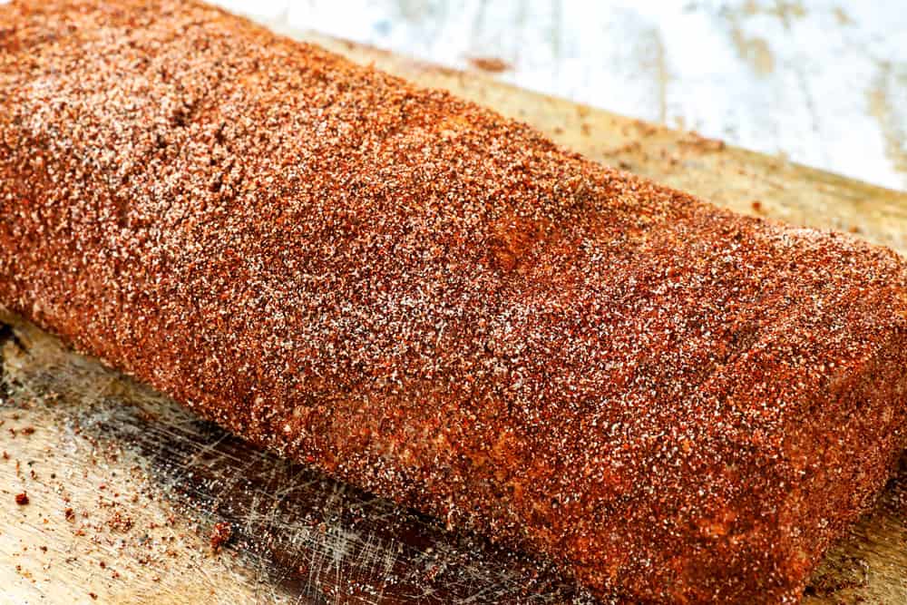 showing how to make pork loin roast by rubbing the pork loin with spices