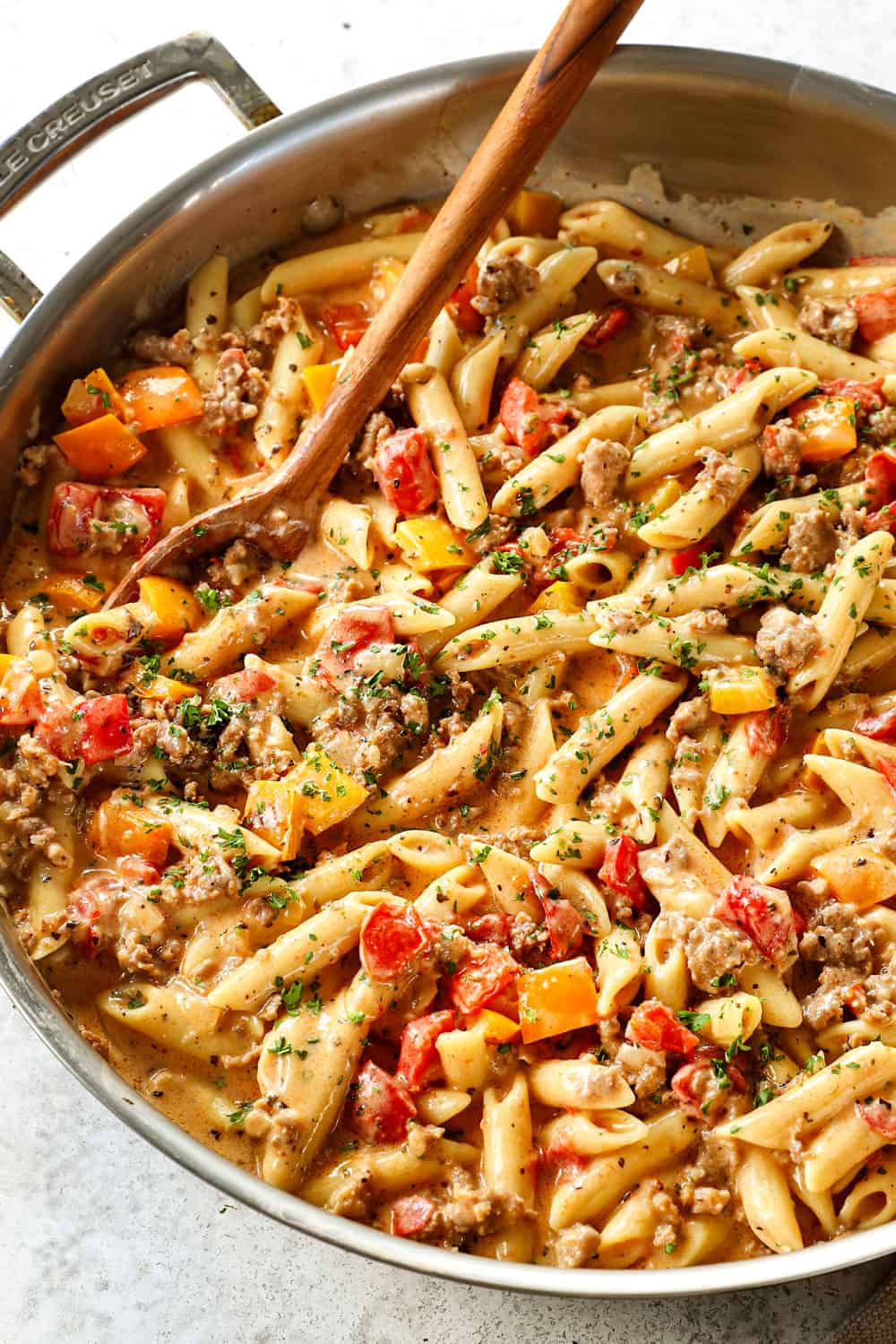 showing how to make Italian sausage pepper pasta recipe by combining pasta, sausage, peppers and sauce in a skillet