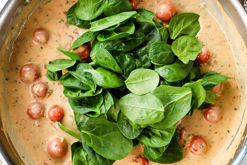 showing how to make Creamy Tuscan shrimp by stirring spinach into the sauce to wilt