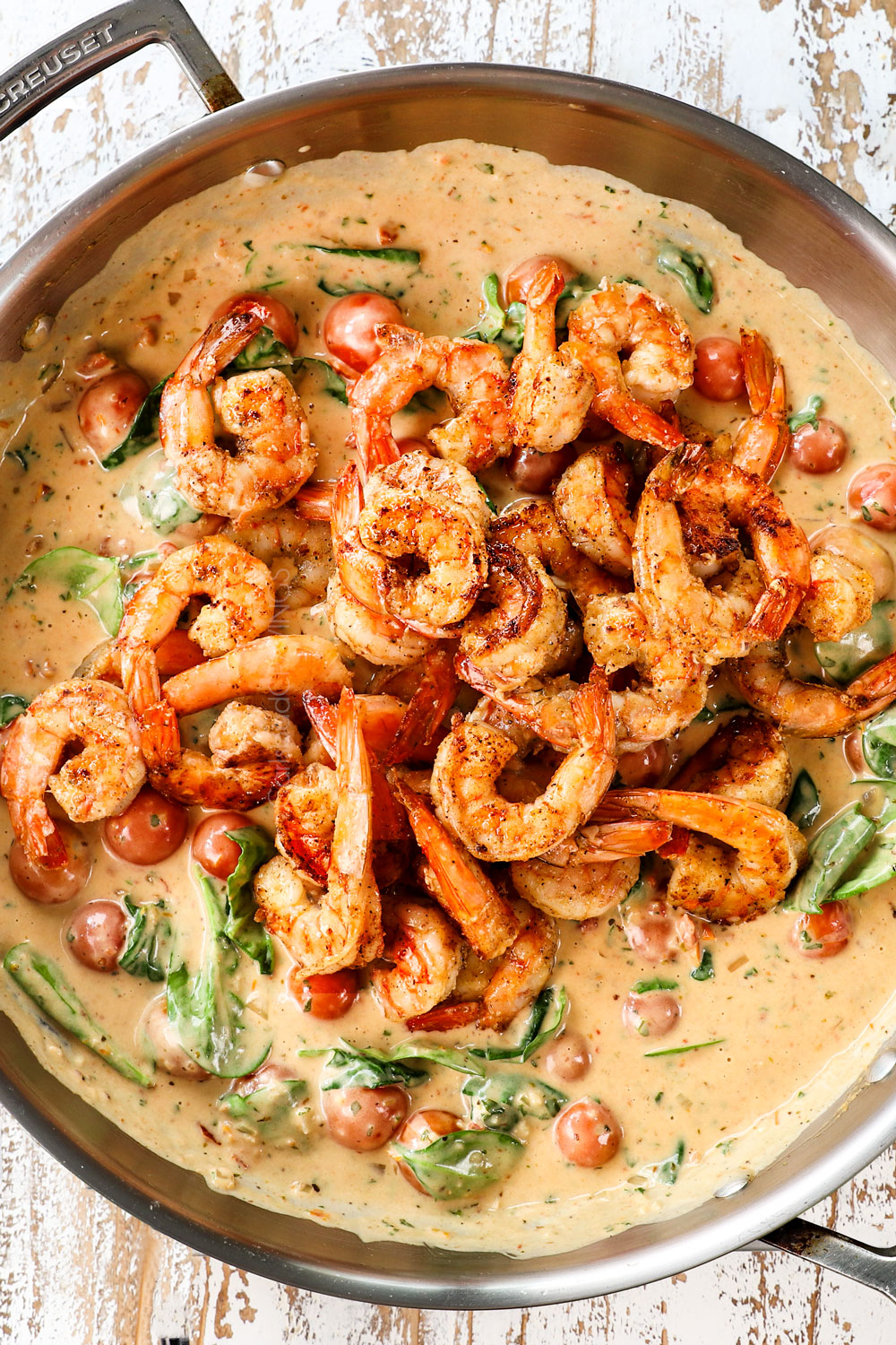 showing how to make garlic creamy Tuscan shrimp by adding the cooked shrimp back to the sauce in the skillet