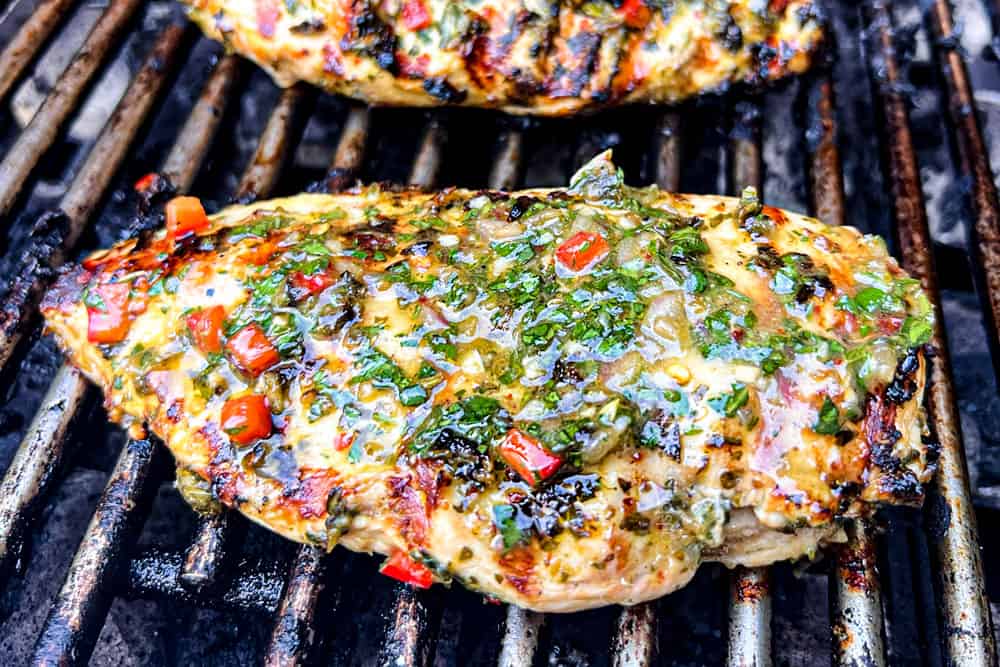 showing how to make chicken chimichurri by grilling the chicken on an outdoor grill and basting with chimichurri