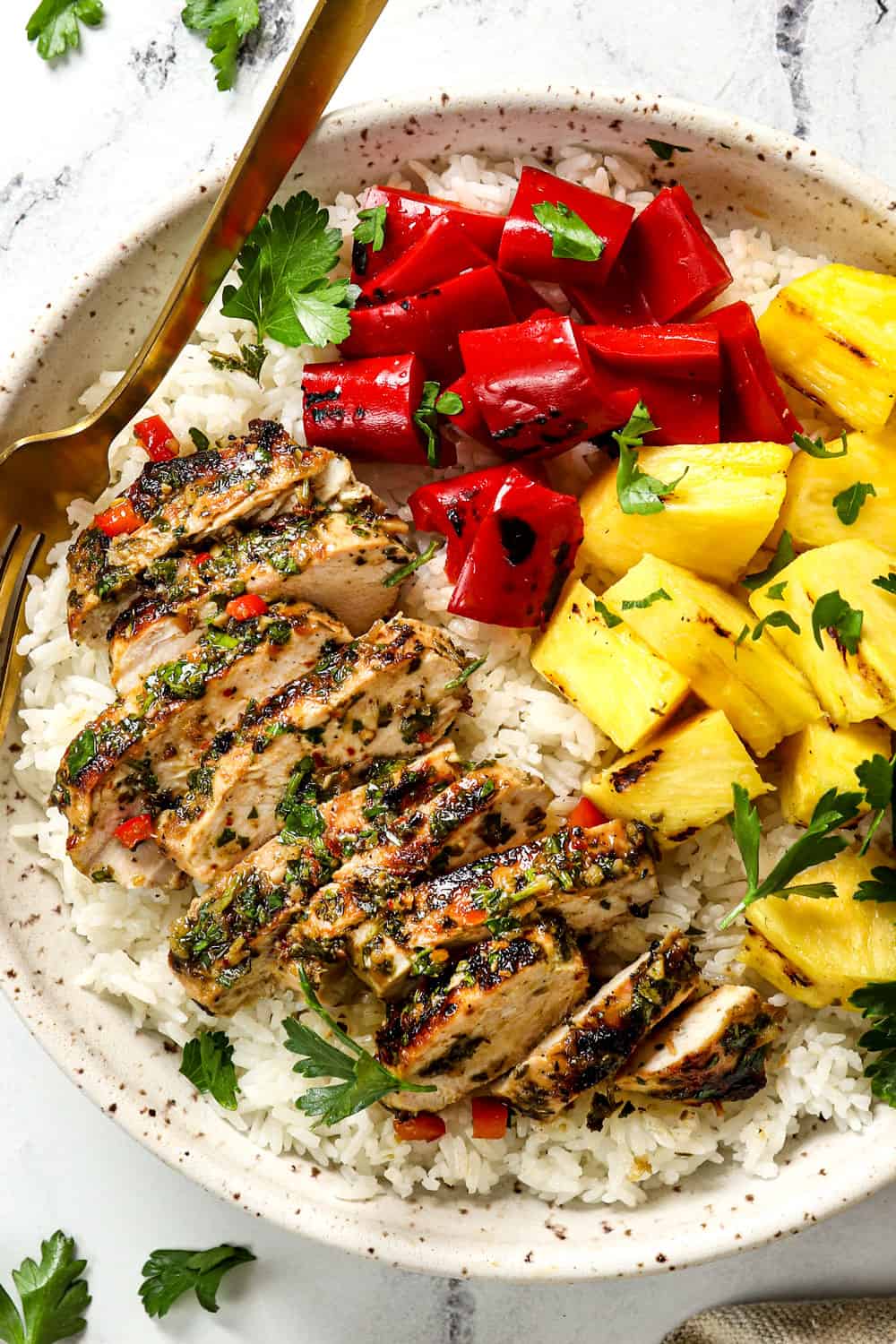 top view showing how to serve chicken chimichurri by adding it to a bowl with rice, pineapple and grilled bell peppers
