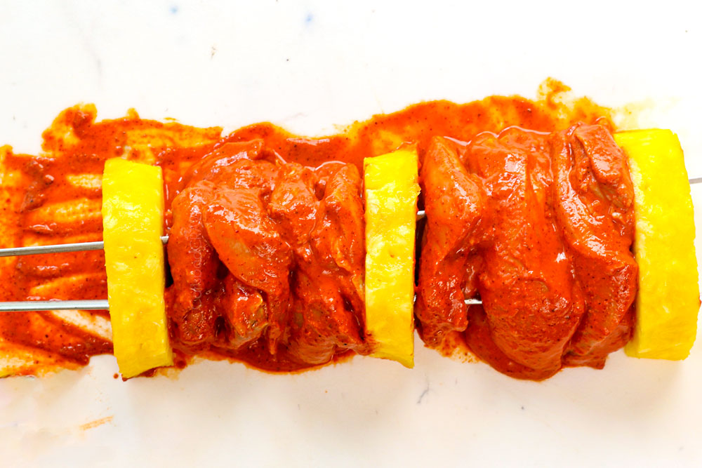 showing how to make al pastor recipe by skewering chicken thighs and pineapple onto two skewers