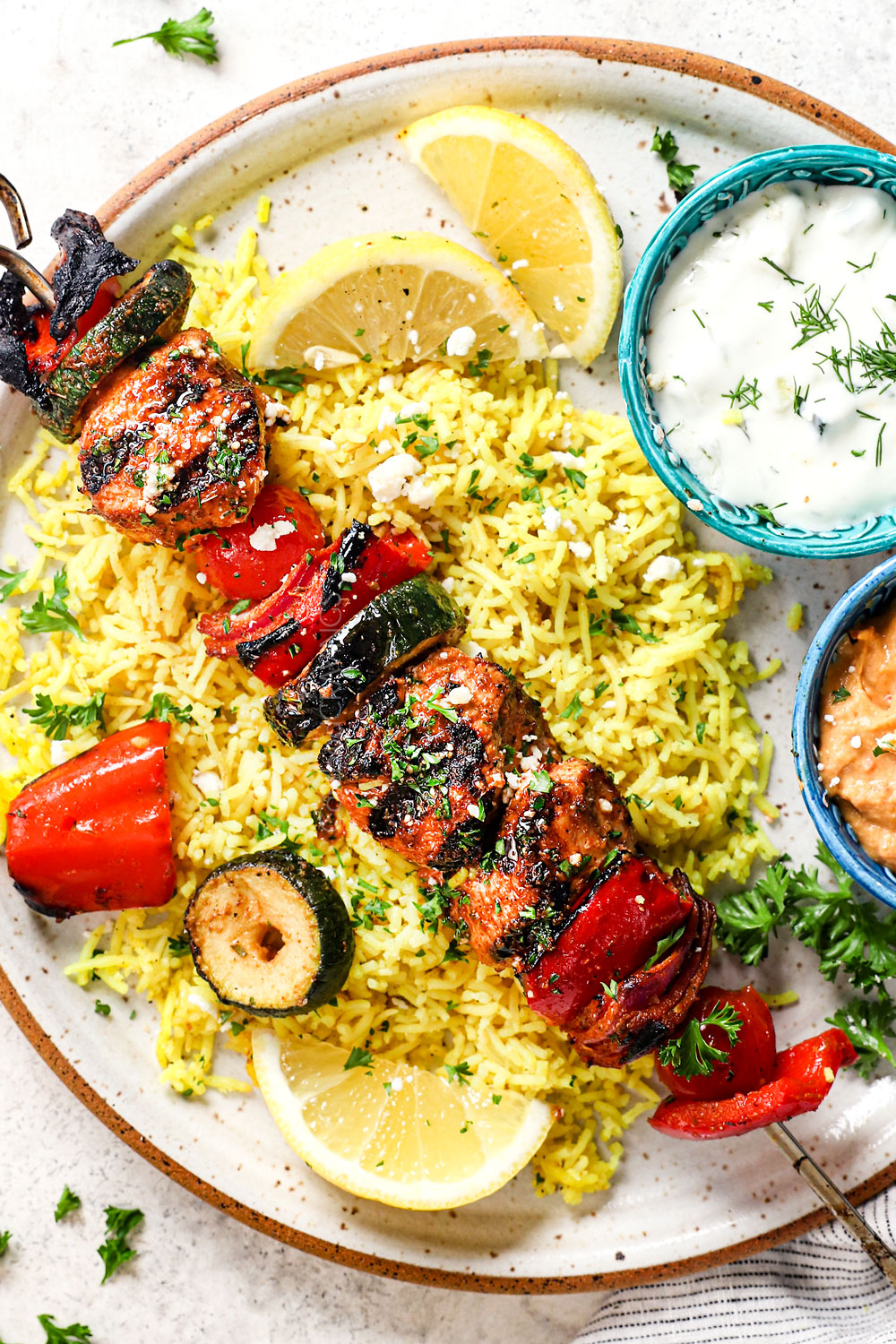 showing how to serve Greek chicken kabobs by adding to a plate with rice and tzatziki sauce