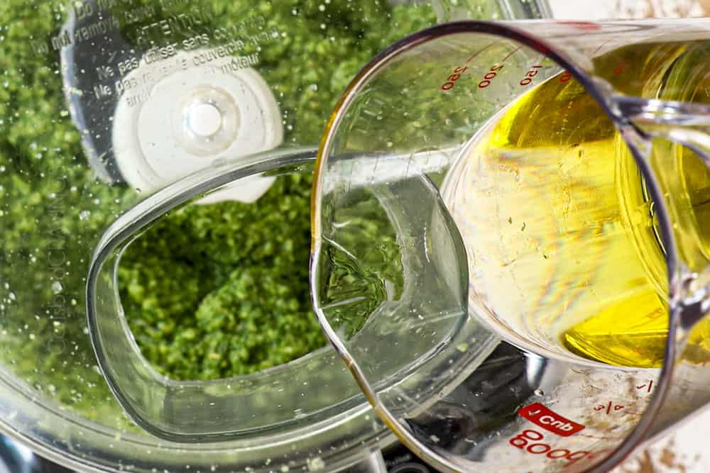 showing how to make pesto by pouring olive oil into food processor while blending pesto