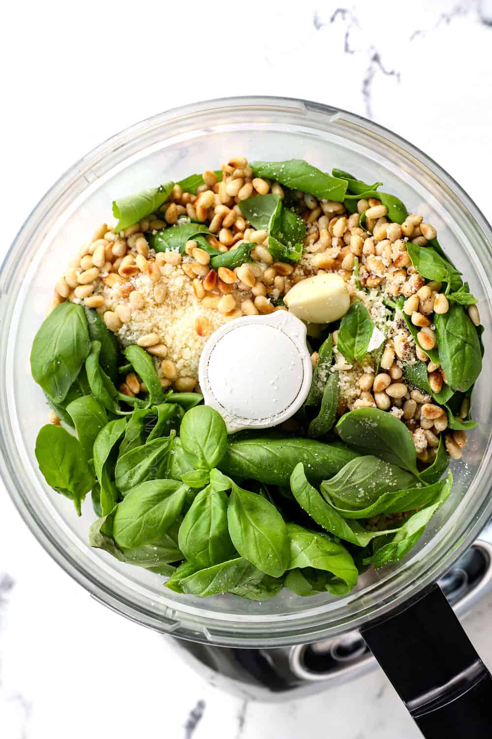 top view showing pesto ingredients in a food processor:  basil, pine nuts, Parmesan and garlic