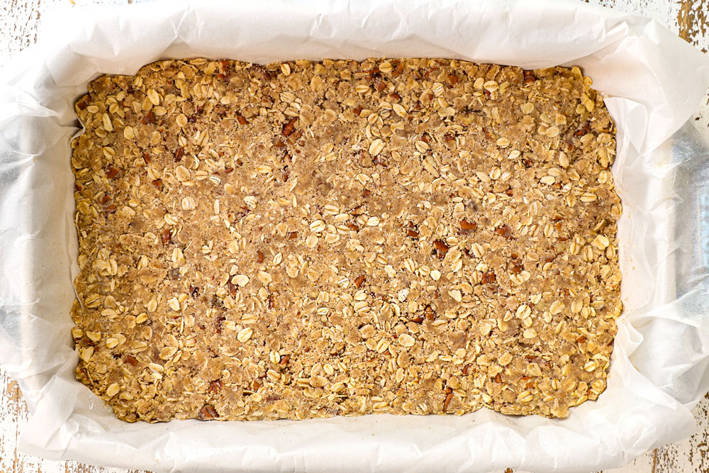showing how to make raspberry bars recipe by adding crumble to a 9x13 baking pan to make the crust