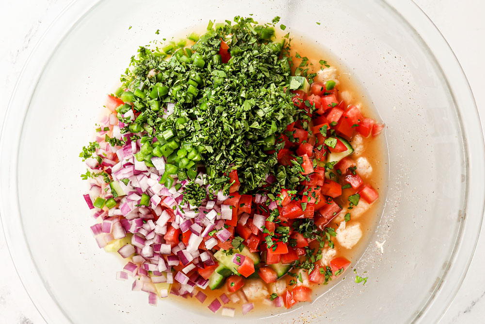showing how to make shrimp ceviche recipe (ceviche de camaron) by adding cilantro, red onions, tomatoes and jalapenos to the shrimp in the bowl