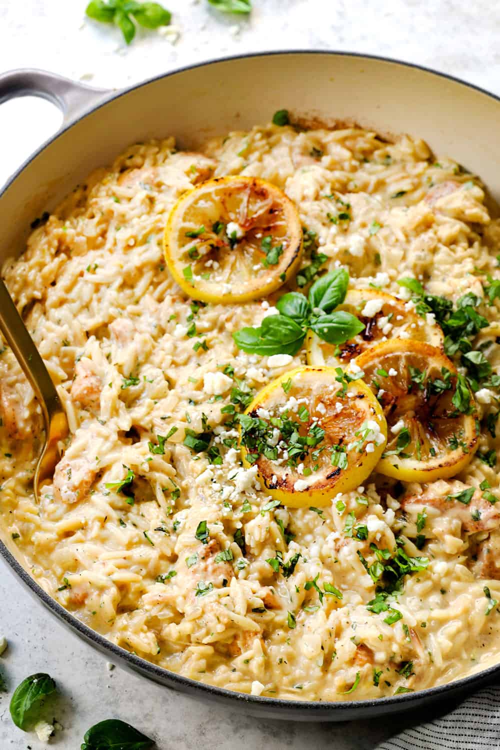 lemon orzo with chicken in a skillet garnished by lemon slices, basil and feta