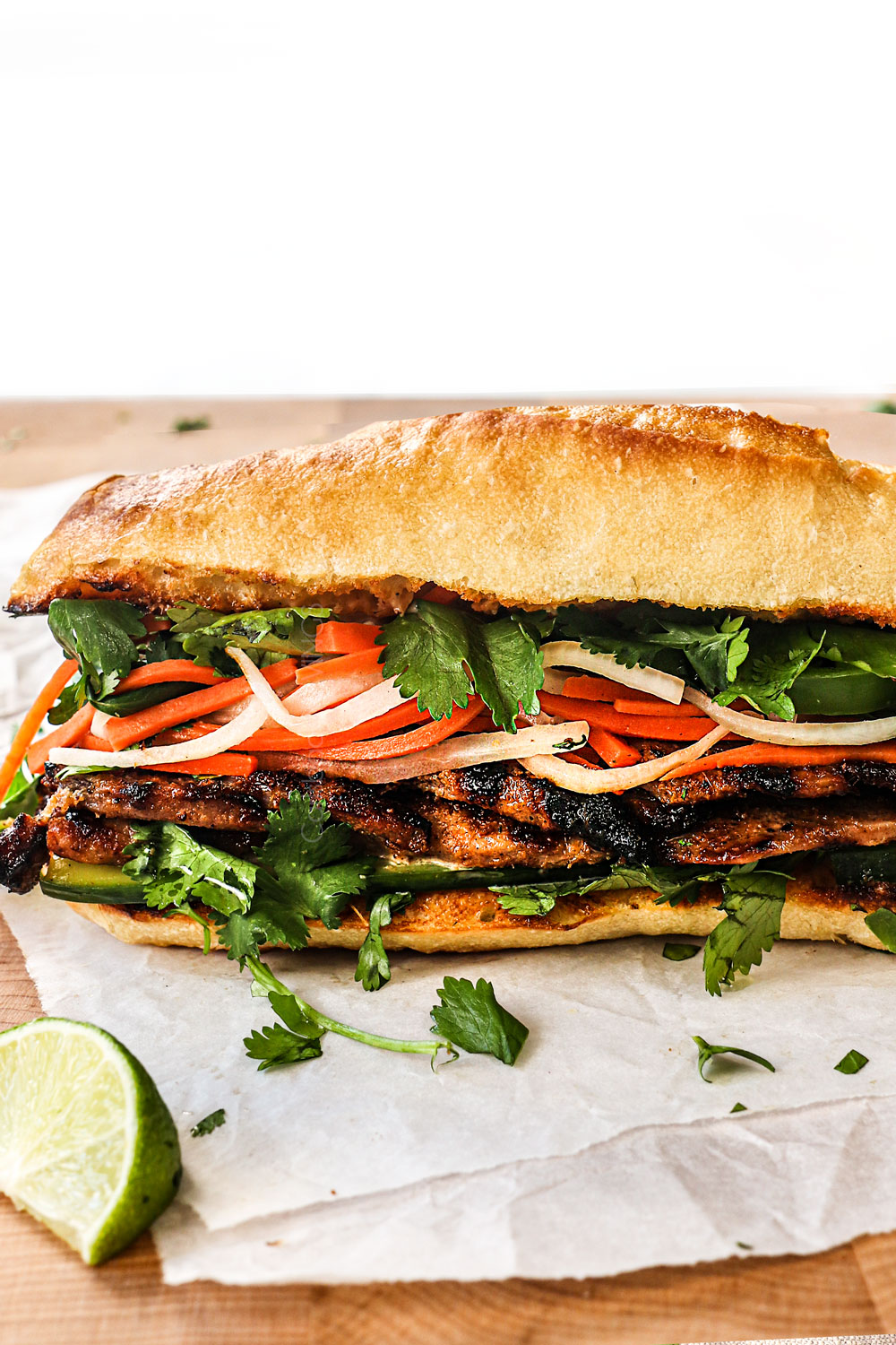 a banh mi sandwich layered with banh mi sauce, pate, grilled pork, cucumber slices, pickled vegetables, jalapenos and cilantro