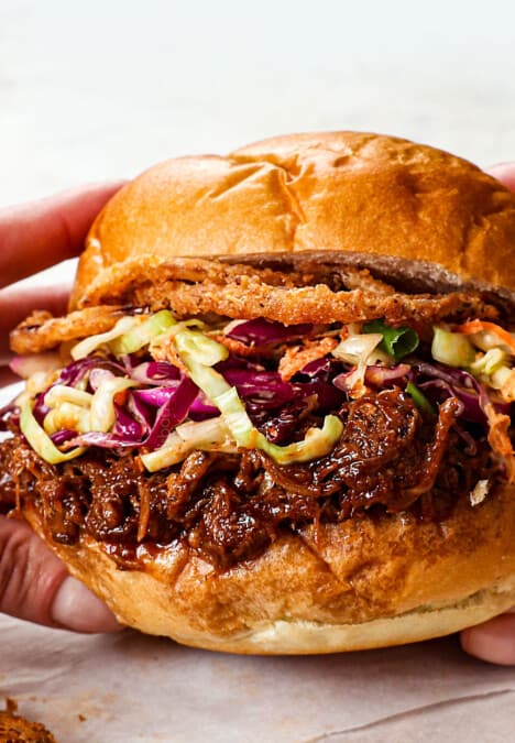 showing how to make BBQ pulled pork sandwiches by topping buns with pulled pork, with coleslaw and fried onion rings