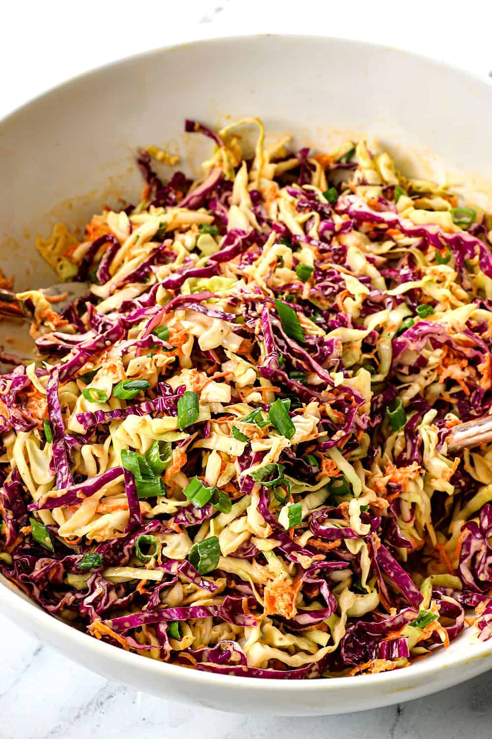 showing how to make pulled pork recipe by tossing cabbage, carrots and green onions with dressing