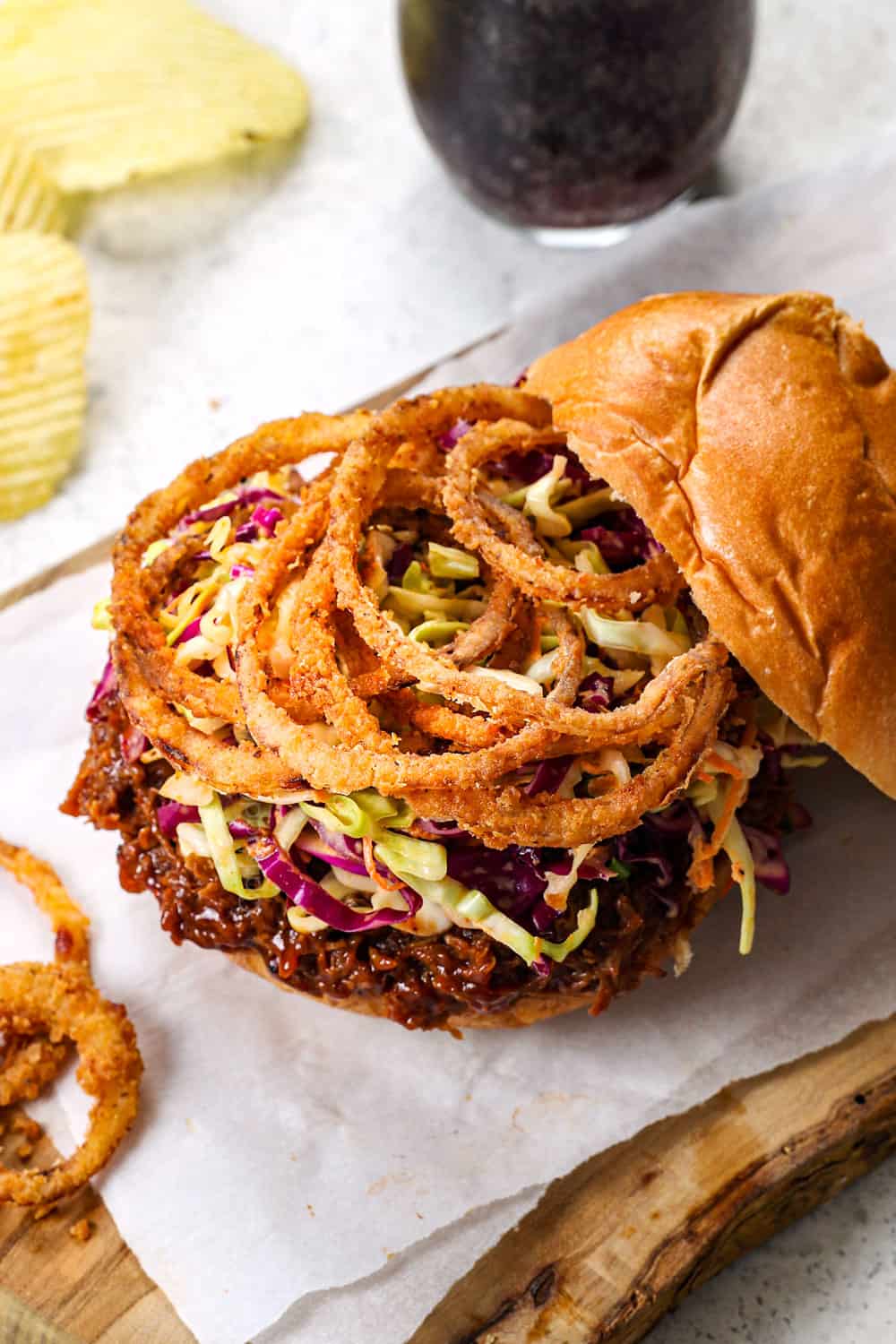 showing how to make BBQ pulled pork sandwiches by adding coleslaw and fried onion rings to BBQ pulled pork
