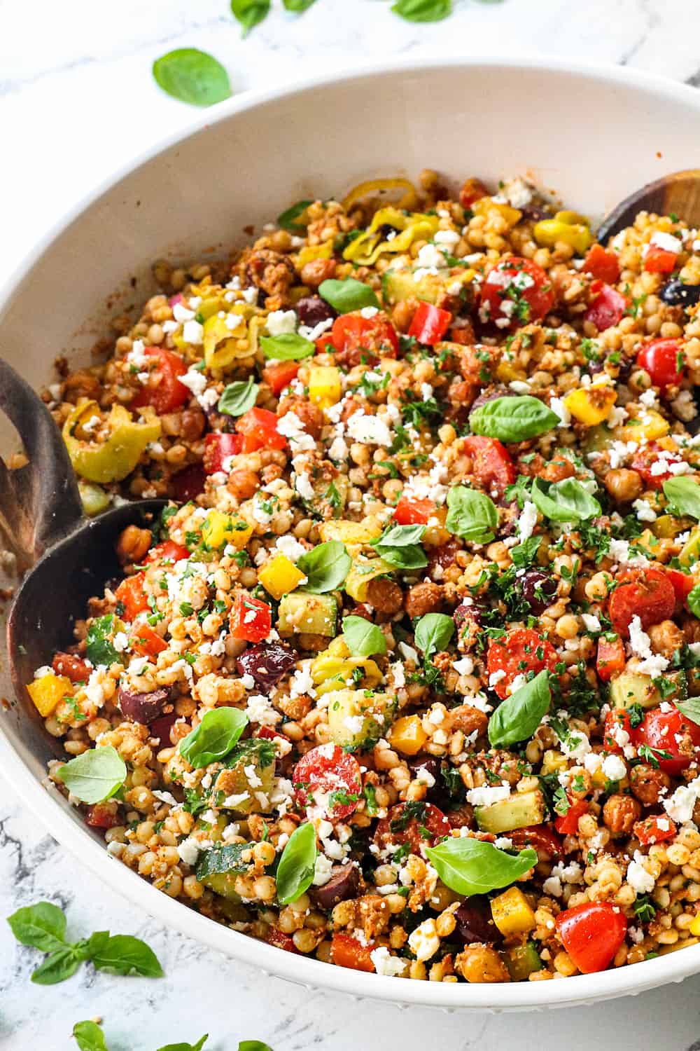 a large bowl of Greek couscous salad recipe with tomatoes, olives, cucumbers, red onions, bell peppers, feta