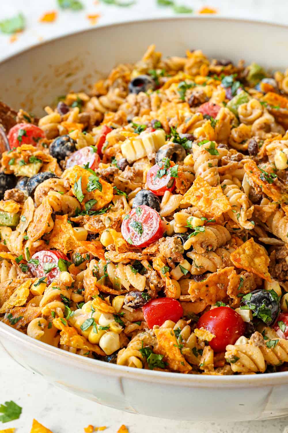 taco pasta salad recipe in a white bowl with ground beef, cheese, lettuce, tomatoes, black beans