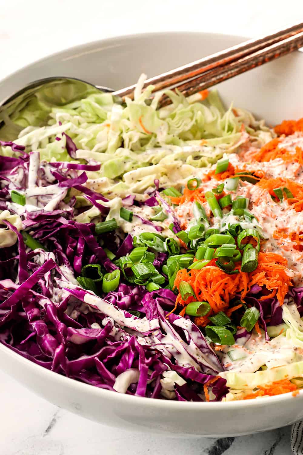 showing how to make traditional coleslaw by drizzling coleslaw dressing over the cabbage