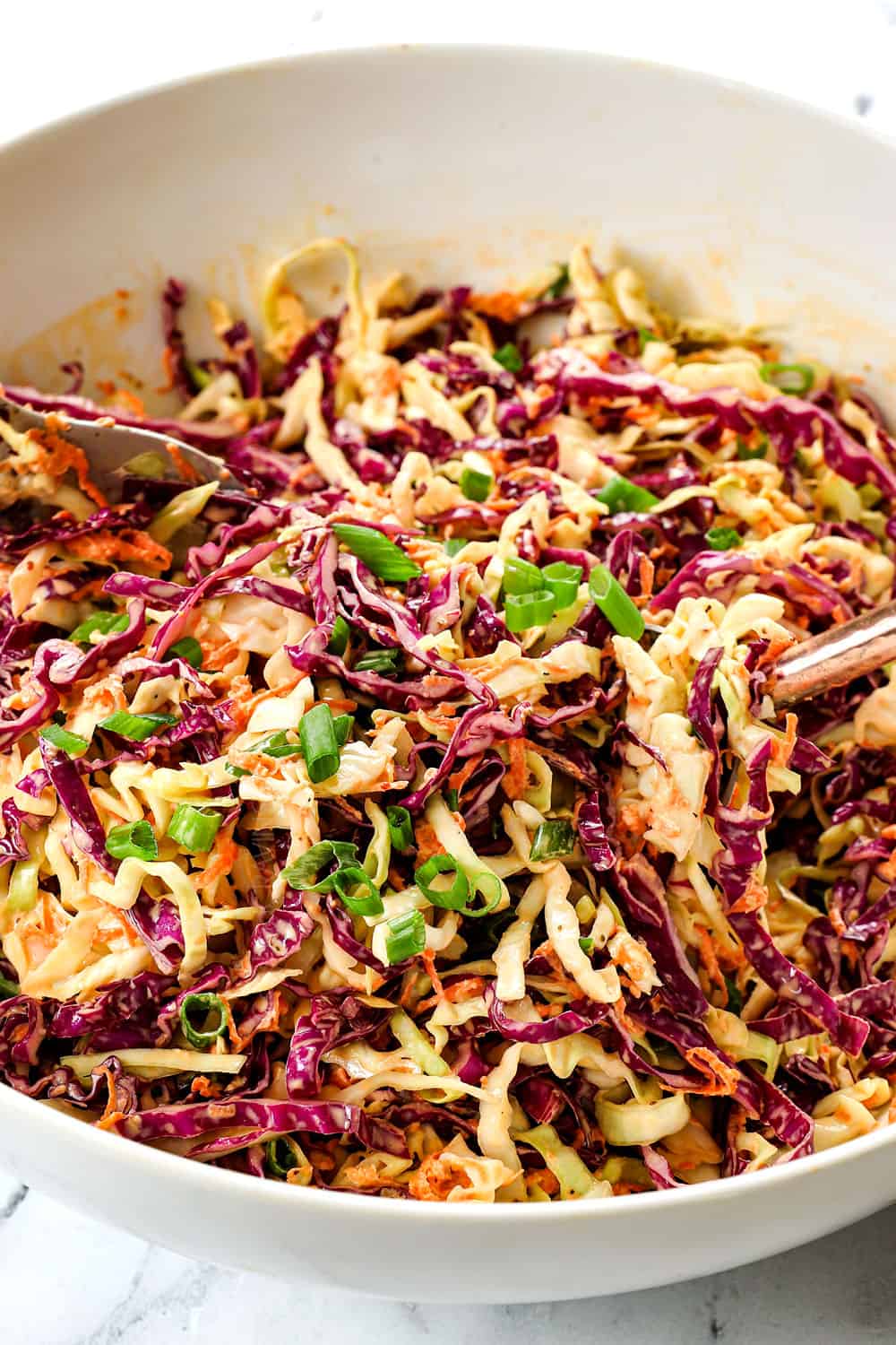 showing how to make coleslaw recipe by tossing all of the coleslaw ingredients together