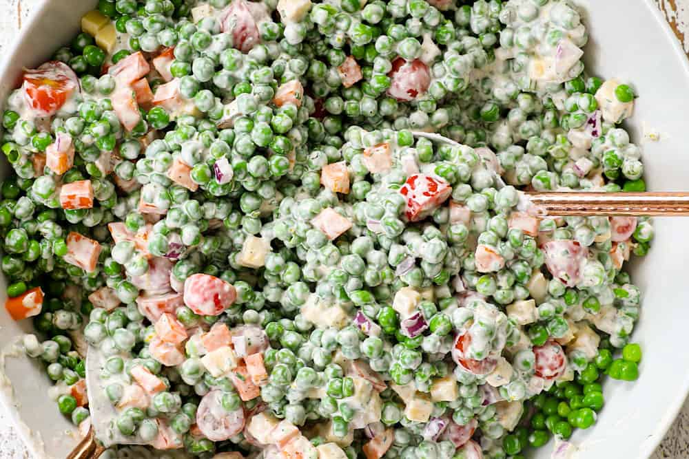 showing how to make pea salad recipe by tossing peas, bacon and cheese together with the dressing in a bowl