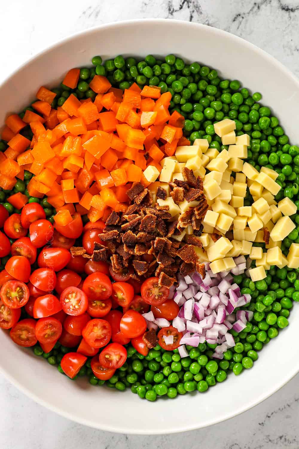 top view showing how to make pea salad by adding green peas, tomatoes, cheese, bacon, bell peppers and red onions to a big bowl