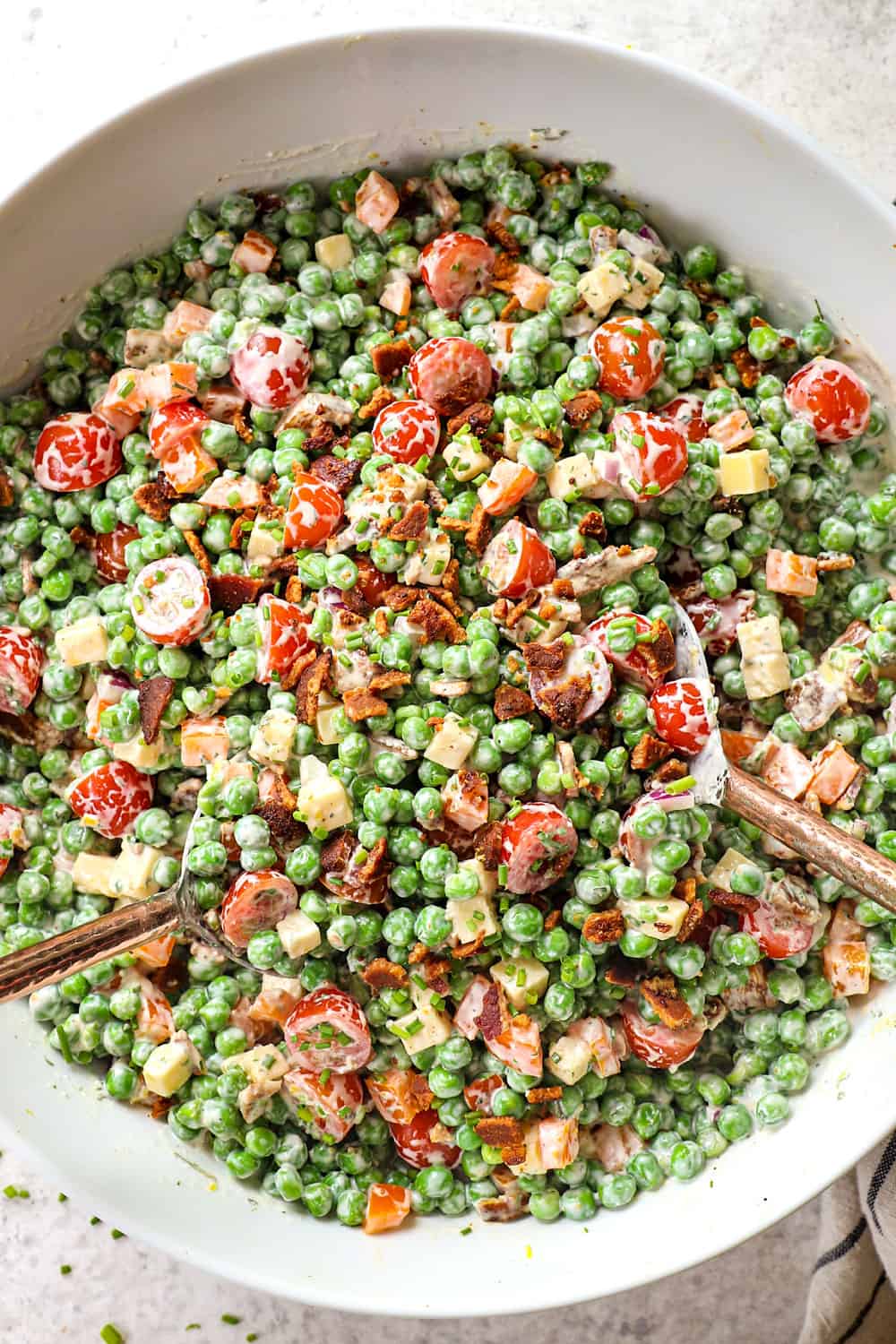 showing how to make pea salad recipe by tossing peas, bacon, cheese, onions, and creamy dressing together in a bowl