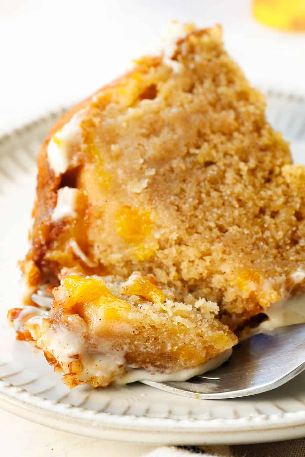 a slice of peach cake recipe with a fork taking a bite showing chunks of peaches