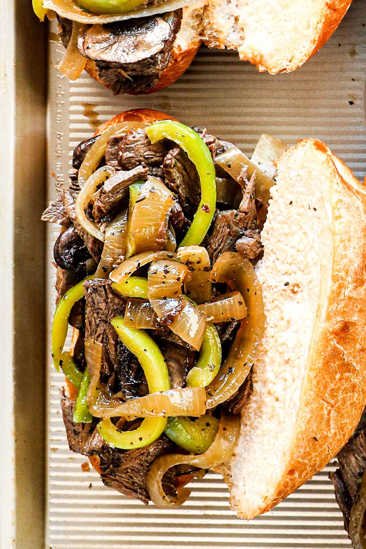 showing how to make Crockpot Philly cheesesteak recipe by adding sliced steak, bell peppers, onions, and mushrooms to a toasted hoagie bun before adding cheese