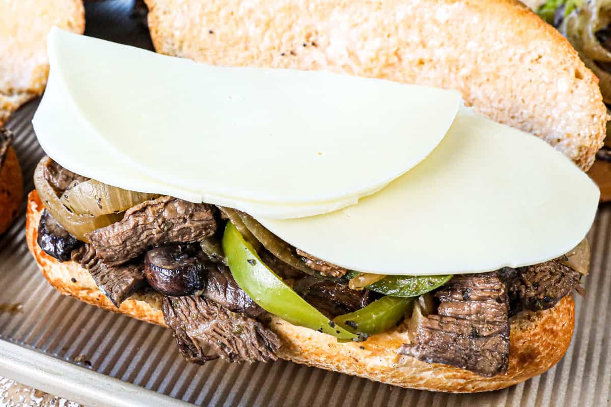 showing how to make Crockpot Philly cheesesteak recipe by adding steak, mushrooms, bell peppers and provolone cheese