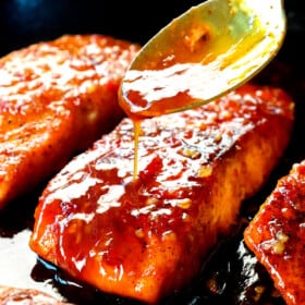 showing how to make firecracker salmon by pouring the sauce over top the pan seared salmon