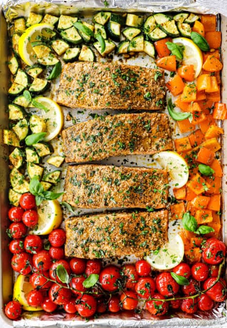 adding pesto salmon to a baking dish with tomatoes, zucchini and bell peppers