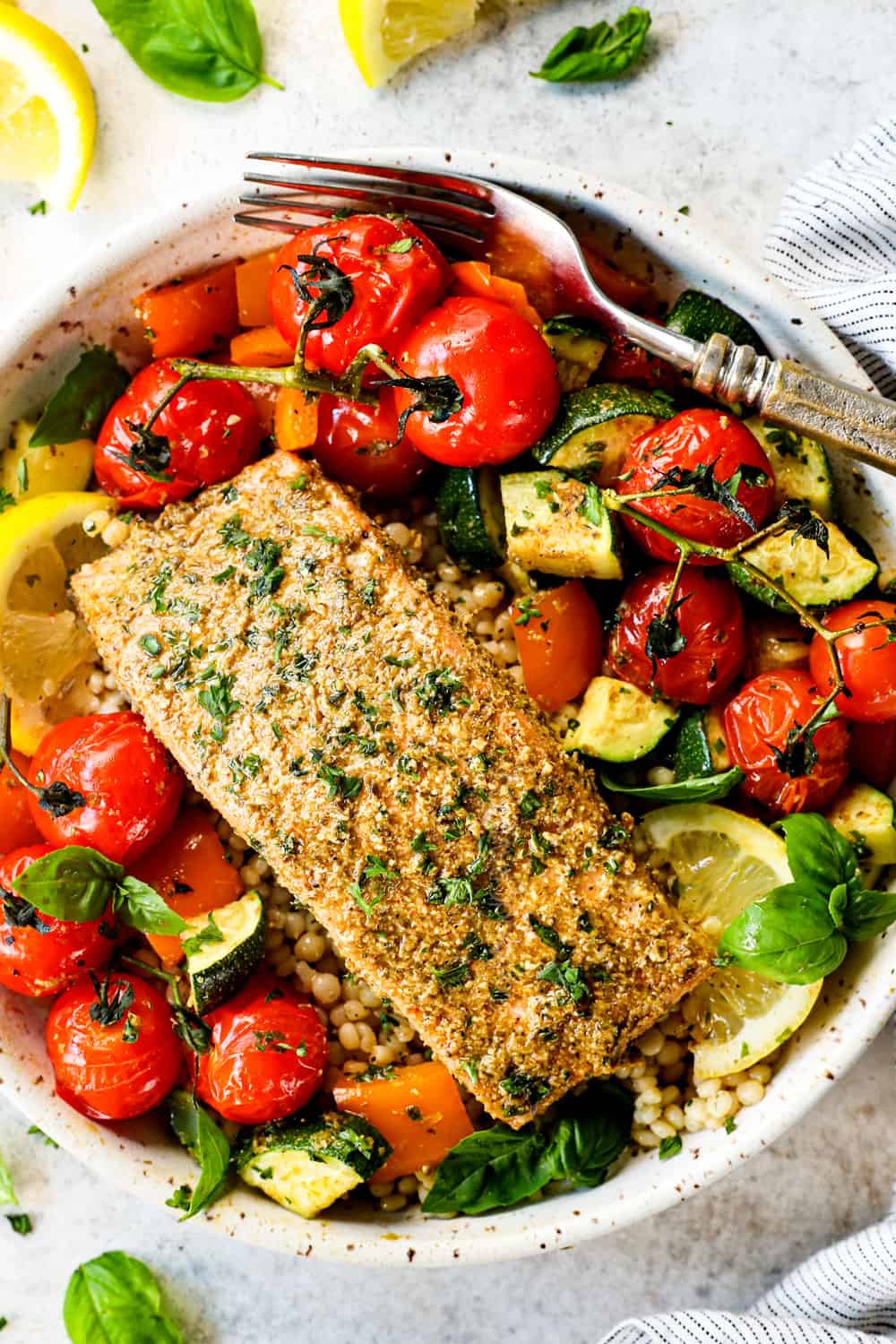 showing how to serve bakes salmon pesto by adding salmon fillets to a blow with rice, tomatoes, zucchini and bell peppers