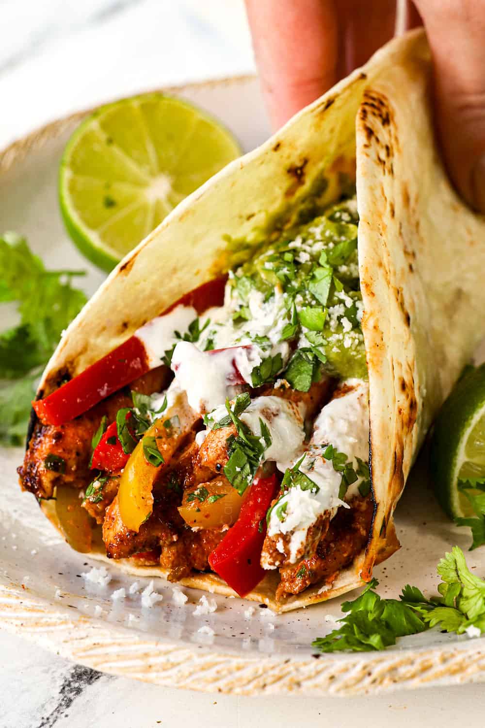 showing how to serve chicken fajitas by adding chicken and strips to a tortilla and topping with sour cream and cilantro