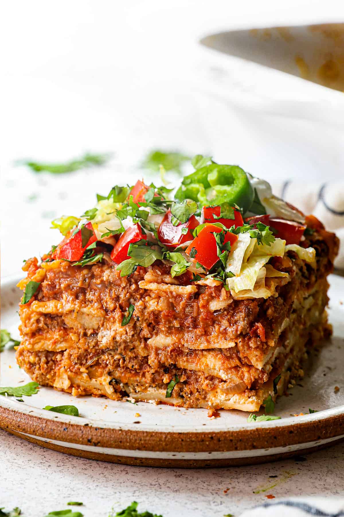 up close of a slice of taco lasagna showing how to serve with lettuce, tomatoes and cilantro