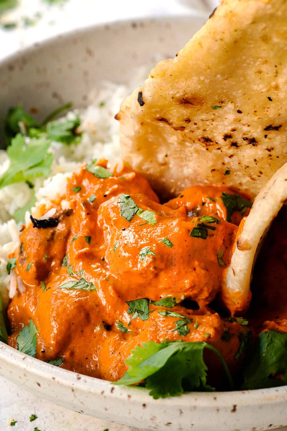 showing how to serve chicken tikka masala by scooping up the chicken and sauce with naan bread
