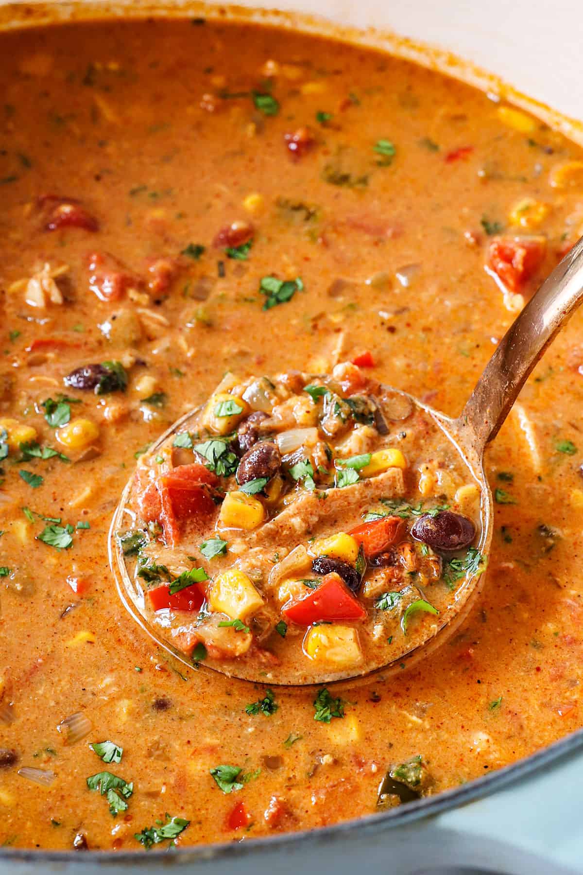 up close of creamy chicken tortilla soup in a pot with chicken, beans, corn and tomatoes in a rich and creamy, cheesy broth
