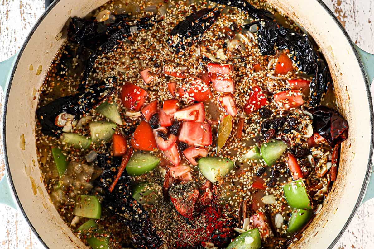 showing how to make Chicken Mole Enchiladas by adding chili peppers, raisings, spices, tomatoes, tomatillos, sunflower seeds, almonds, tomatoes and chicken broth to a pot to simmer