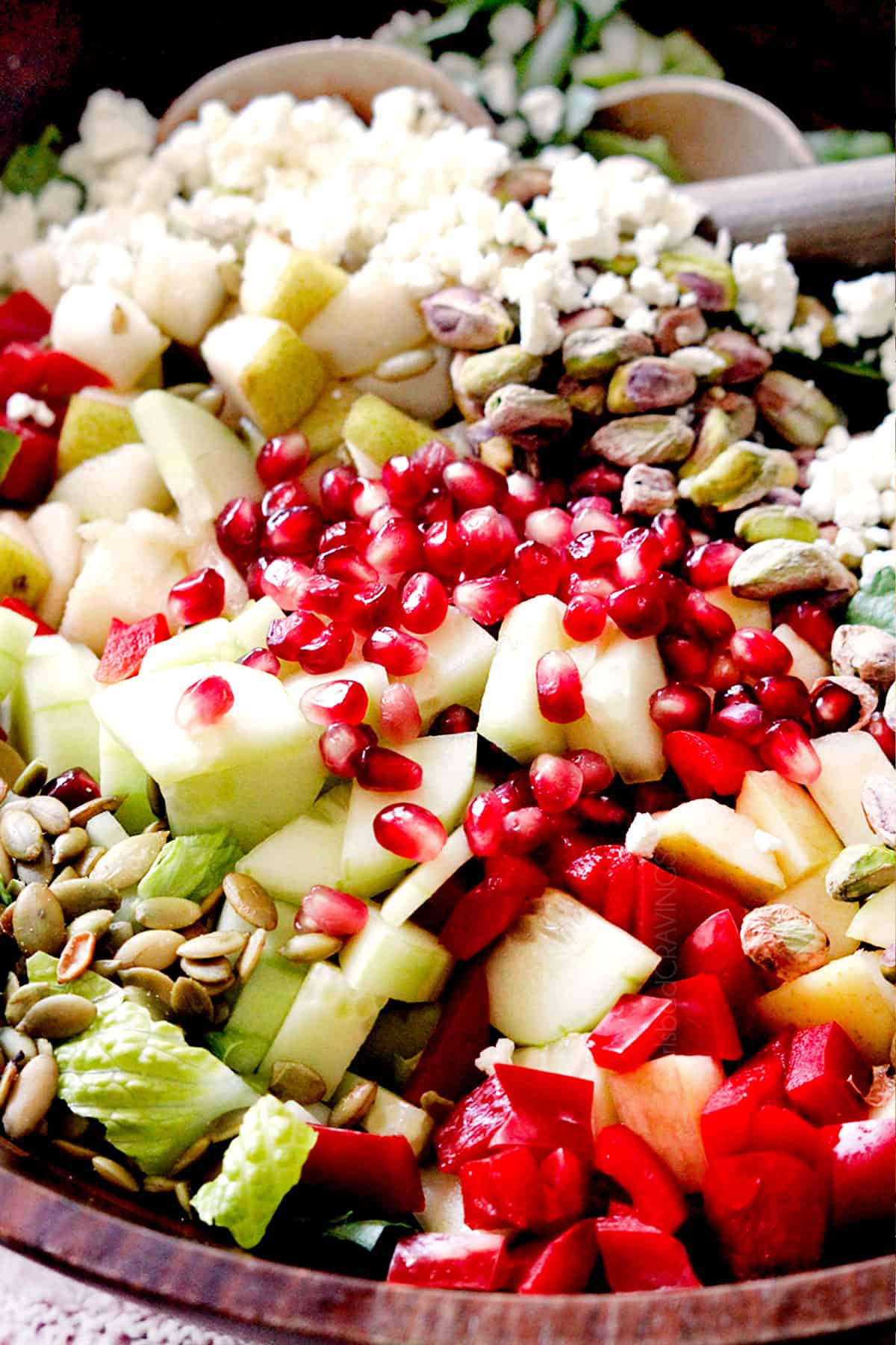 showing how to make pear salad with up close of ingredients in a bowl:  pears, gorgonzola, pomegranate seeds, walnuts, cucumbers, red bell pepper and pepitas