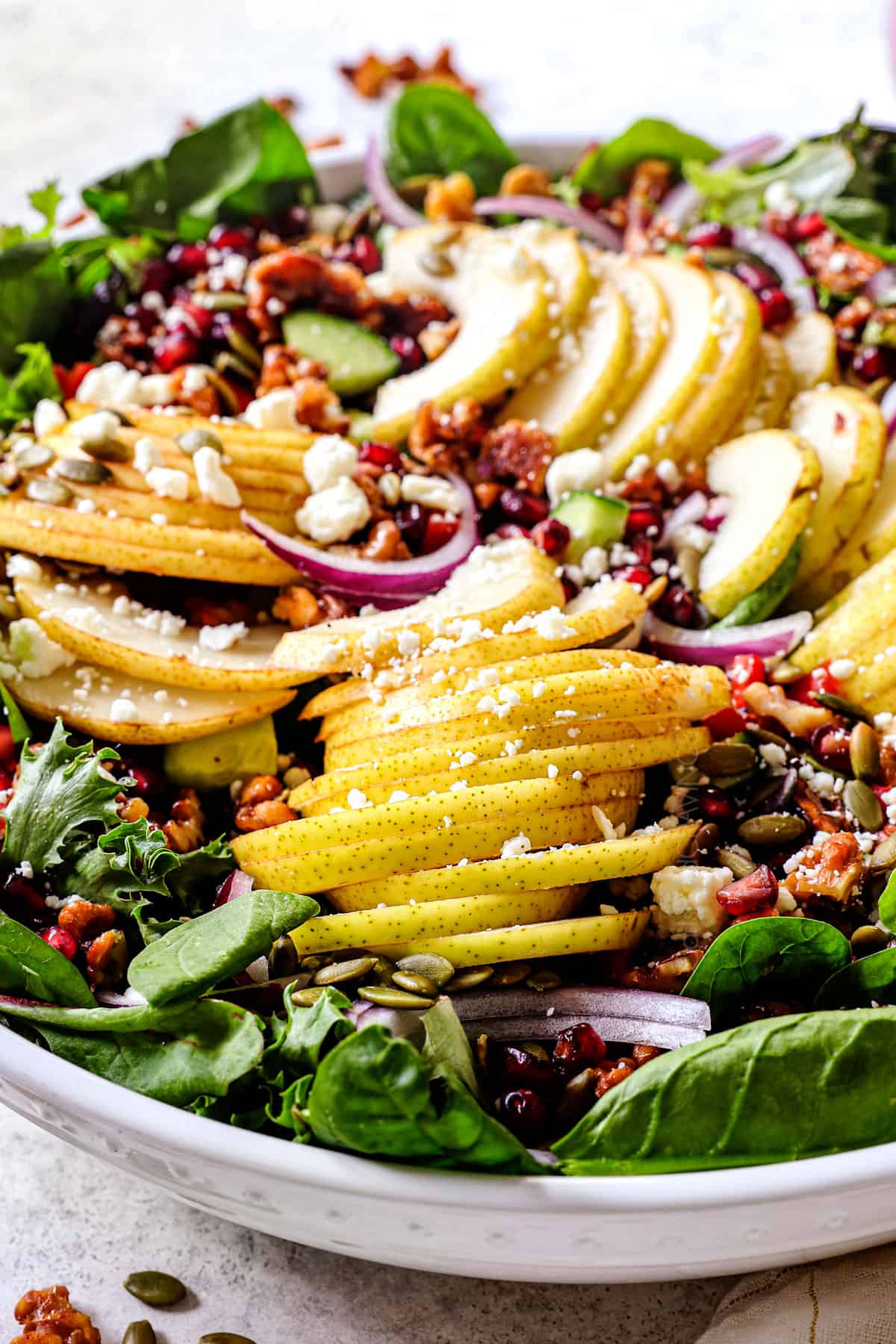 showing how to make pear salad by adding sliced pear to a bowl with spinach, and walnuts