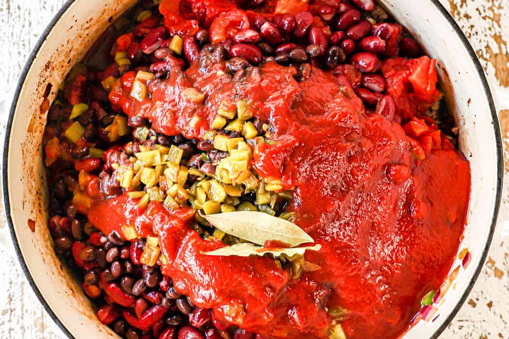 showing how to make pumpkin chili recipe by adding pumpkin puree, tomato sauce, green chilies, kidney beans, black beans and bay leaves to the soup pot