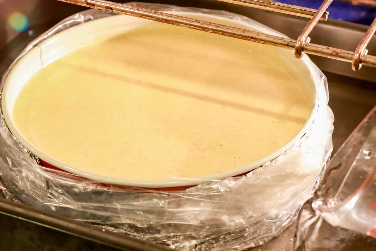 showing how to make caramel apple cheesecake by adding to a roasting pan and adding hot water to make a waterbath